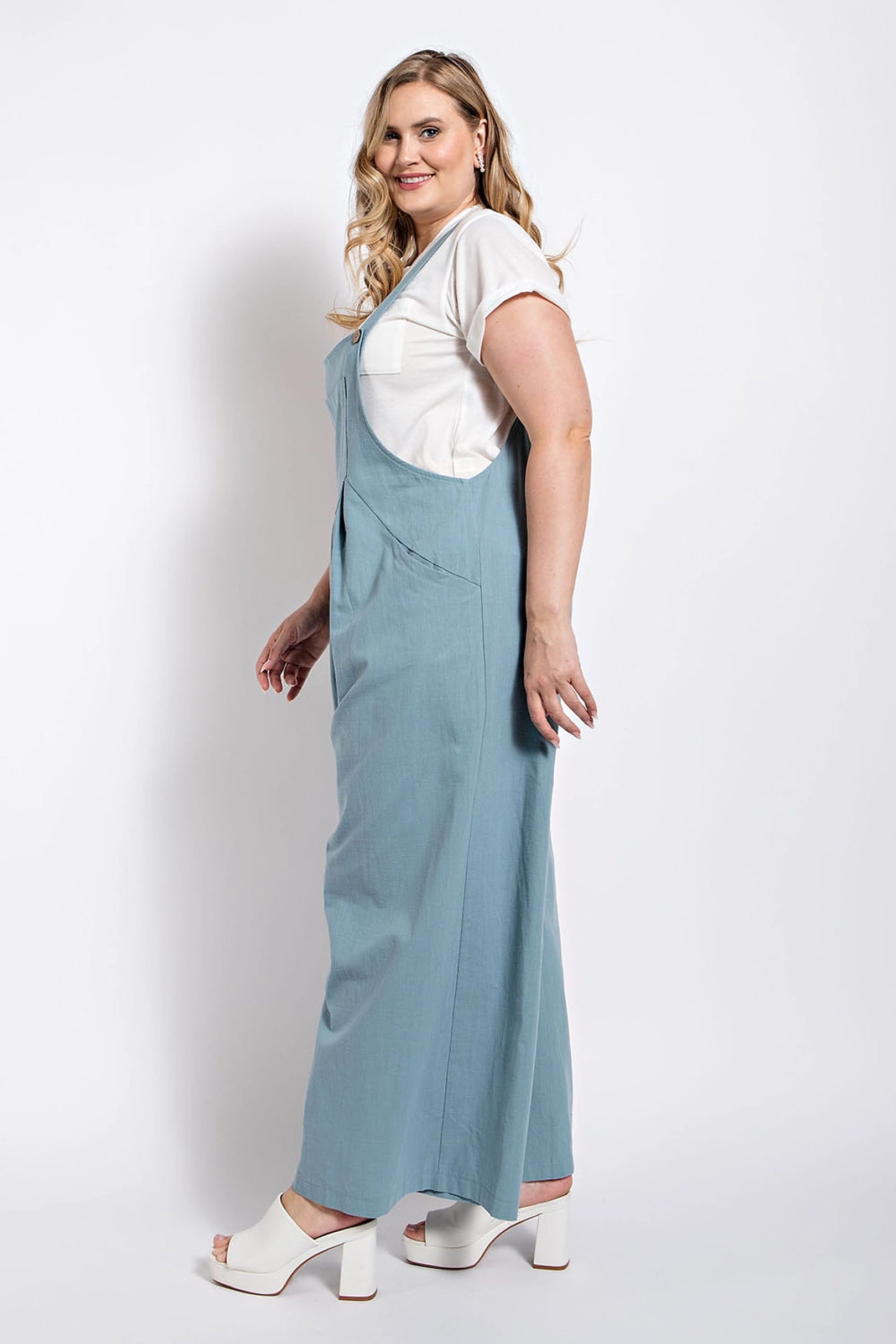 Woman wearing a stone-colored pintuck detail overall with side pockets, styled with a white top and heeled sandals.