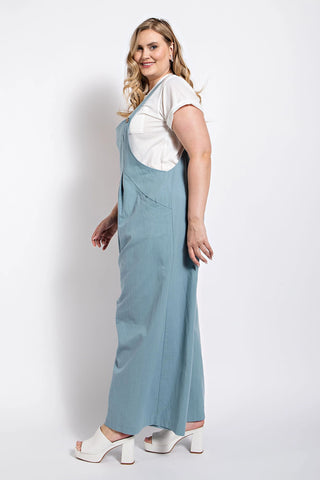 Woman wearing a stone-colored pintuck detail overall with side pockets, styled with a white top and heeled sandals.