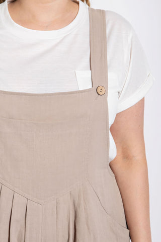 Stone cotton overall with pintuck detail and side pockets worn over white t-shirt, showcasing button strap design.