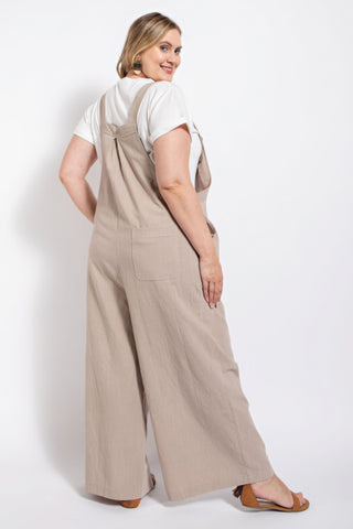 Woman wearing stone-colored pintuck detail overall with side pockets, crafted from cotton, showcasing casual elegance.