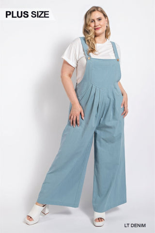 Plus size light denim overall with pintuck detailing and side pockets, styled with a white top and white sandals.