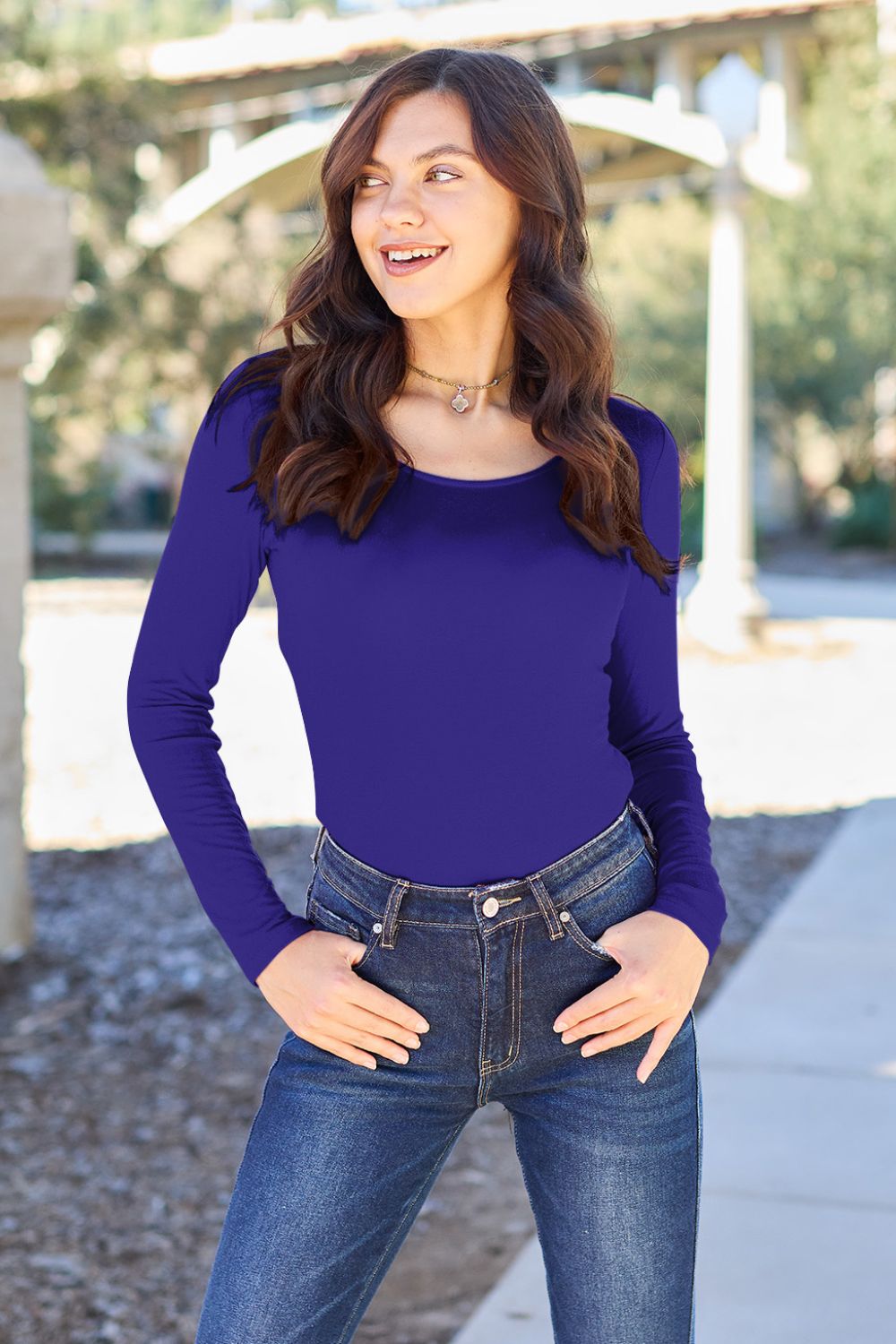 Woman wearing Basic Bae Full Size Round Neck Long Sleeve Bodysuit in blue, paired with jeans, outdoors.