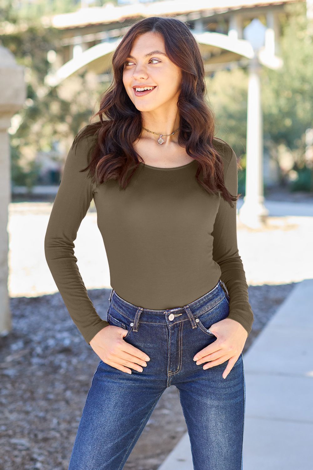 Woman wearing Basic Bae full size round neck long sleeve bodysuit in olive green with jeans, standing outdoors.