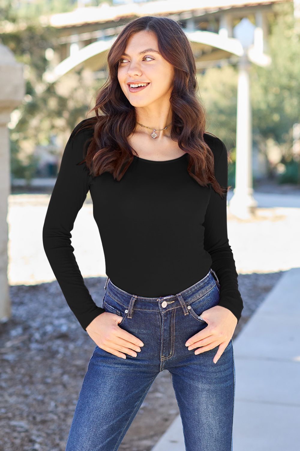 Woman wearing Basic Bae black long sleeve bodysuit with round neck, paired with blue jeans, outdoors.