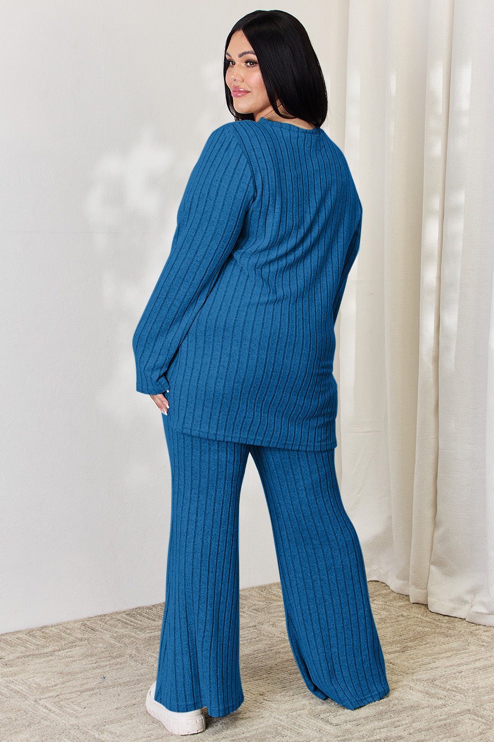 Plus-size model wearing blue ribbed high-low top and wide-leg pants set, showcasing back view of stylish two-piece outfit.