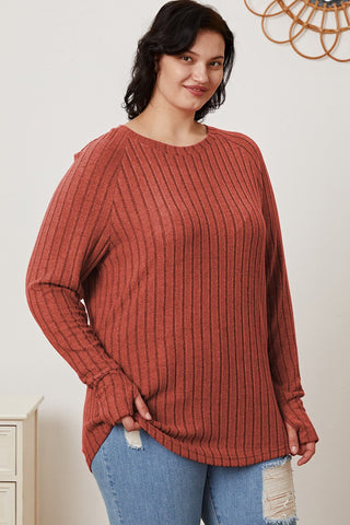 Woman wearing a Basic Bae Full Size Ribbed Thumbhole Sleeve T-Shirt in rust color, paired with ripped jeans, standing indoors.