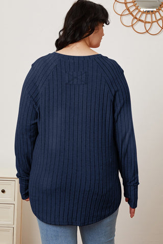 Woman wearing navy blue full-size ribbed thumbhole sleeve t-shirt, viewed from the back, paired with light jeans.