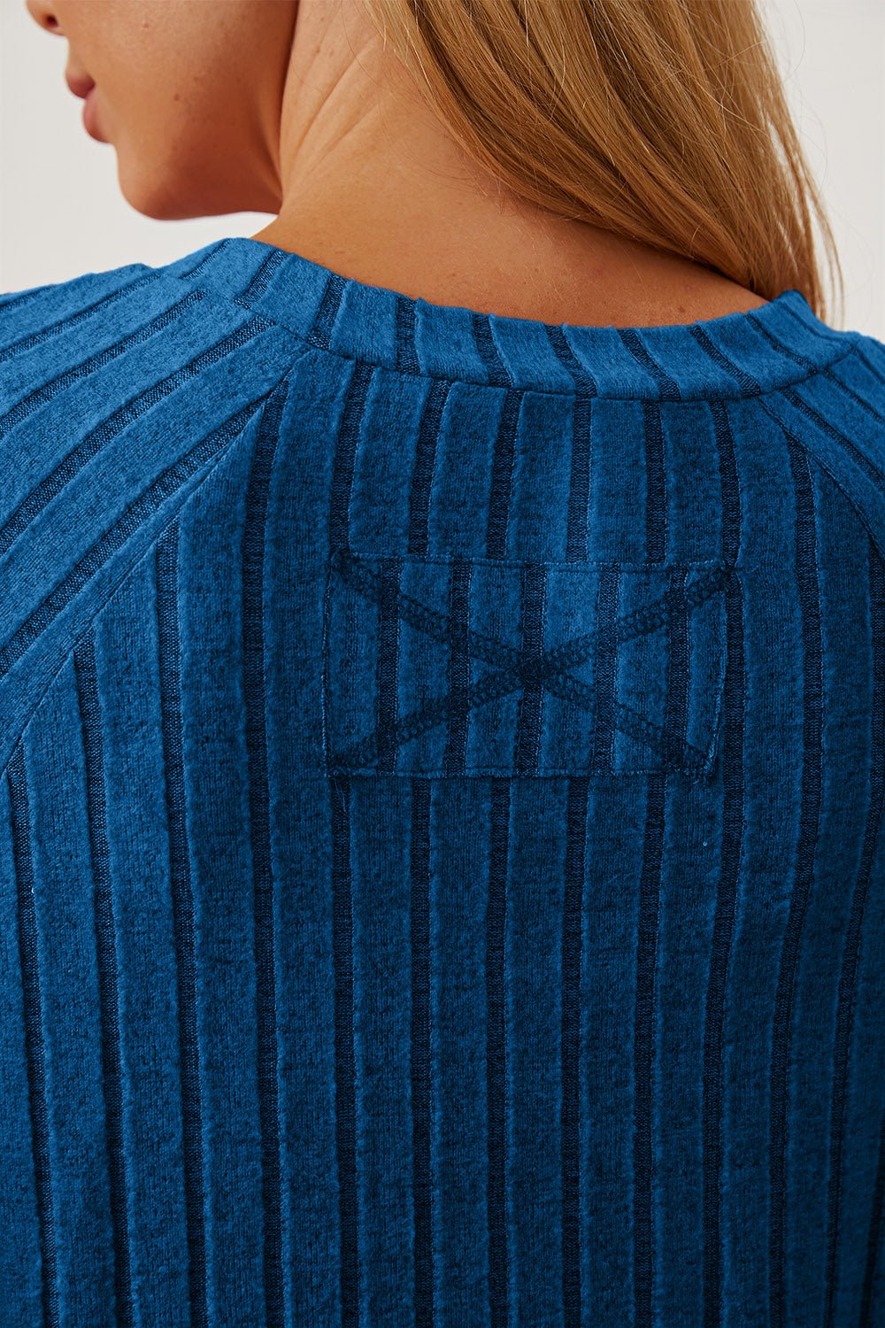 Close-up of blue ribbed t-shirt with thumbhole sleeve detail, back view showing textured fabric and design pattern.