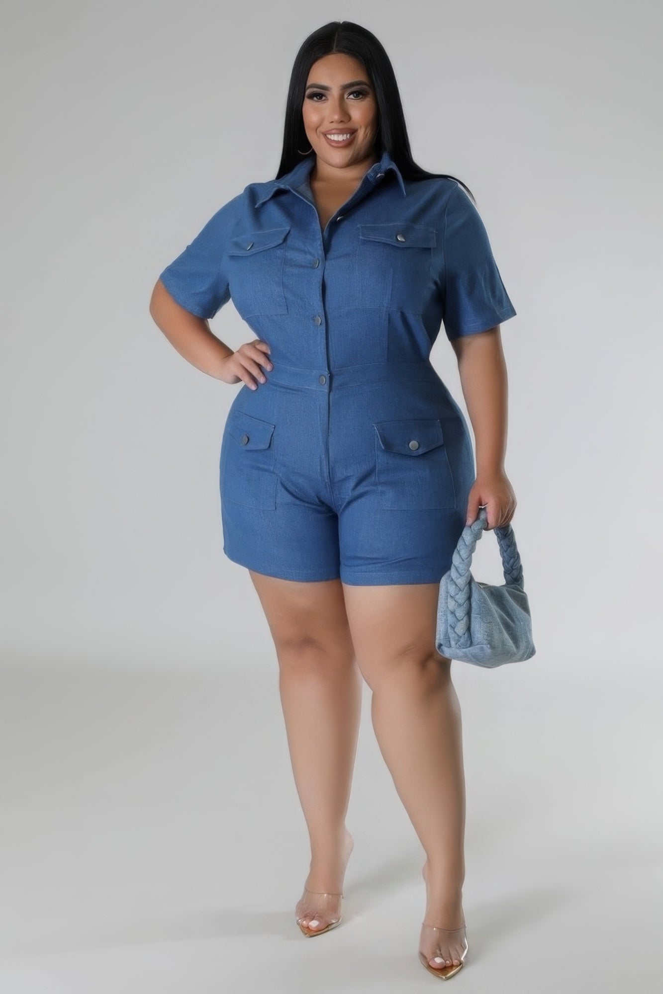 Woman wearing a blue semi-stretch romper with collar, short sleeves, and pockets, holding a matching handbag, showcasing plus size fashion.
