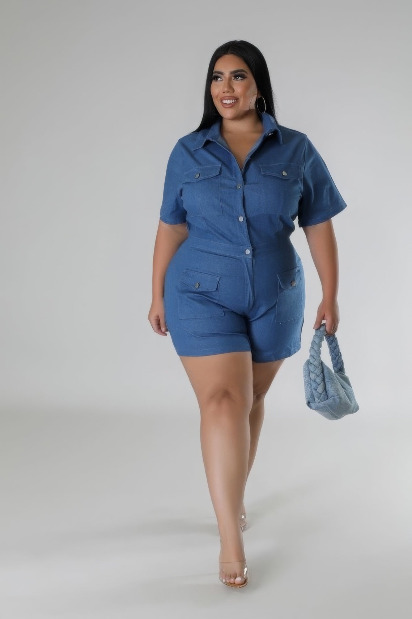 Plus-size model wearing blue semi-stretch romper with collar, short sleeves, pockets, and carrying a matching blue handbag.