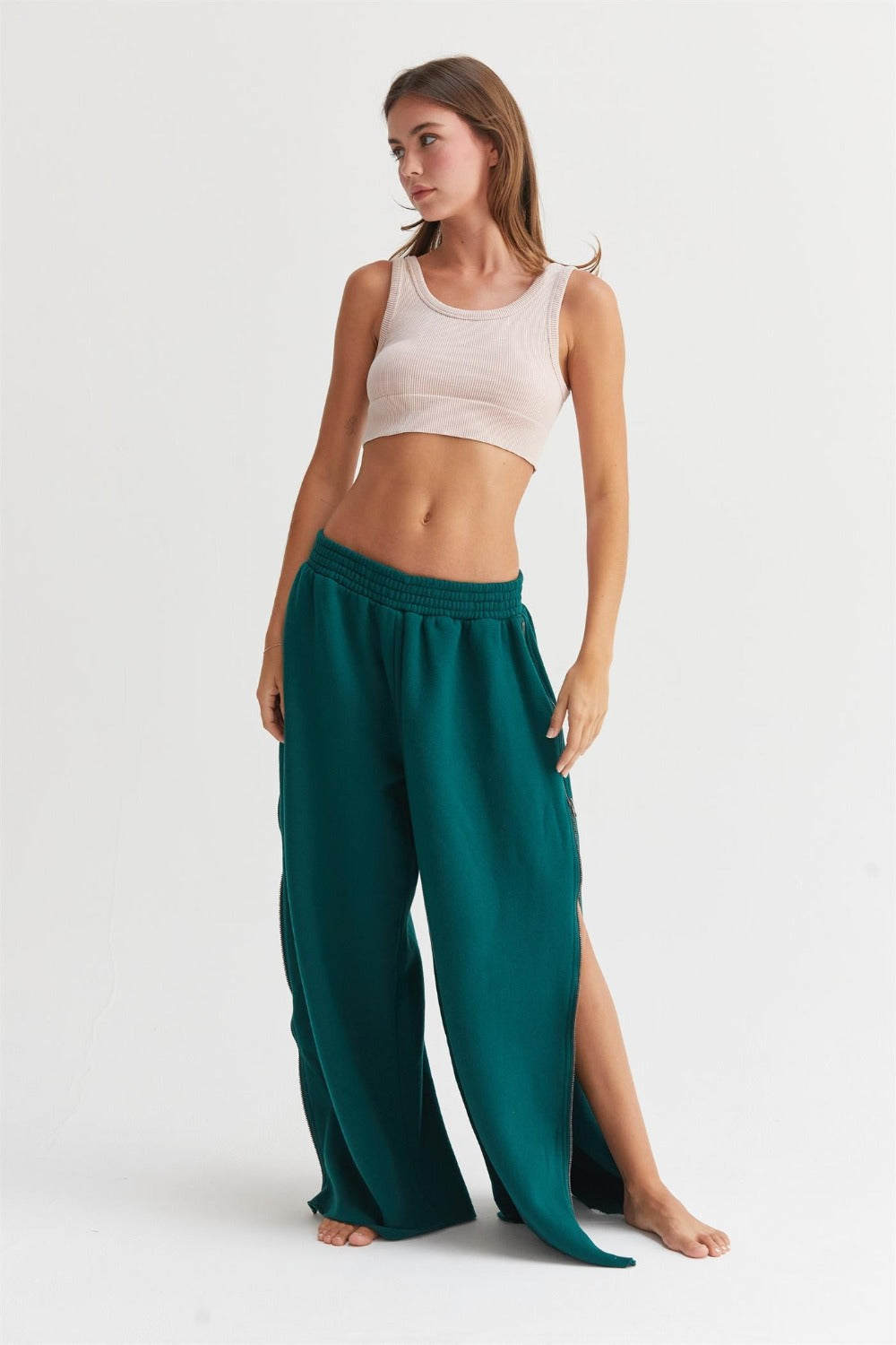 Woman wearing dark green wide-leg sweatpants with side zippers and a beige crop top, showcasing casual comfort and style.