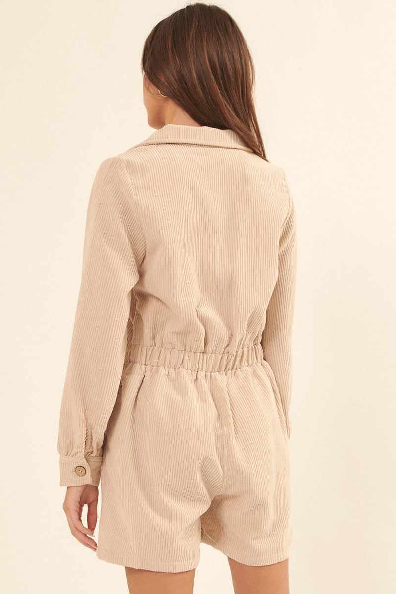 Woman wearing cream woven corduroy romper with lapel collar, elastic waist, and long sleeves, featuring a relaxed fit and side pockets.