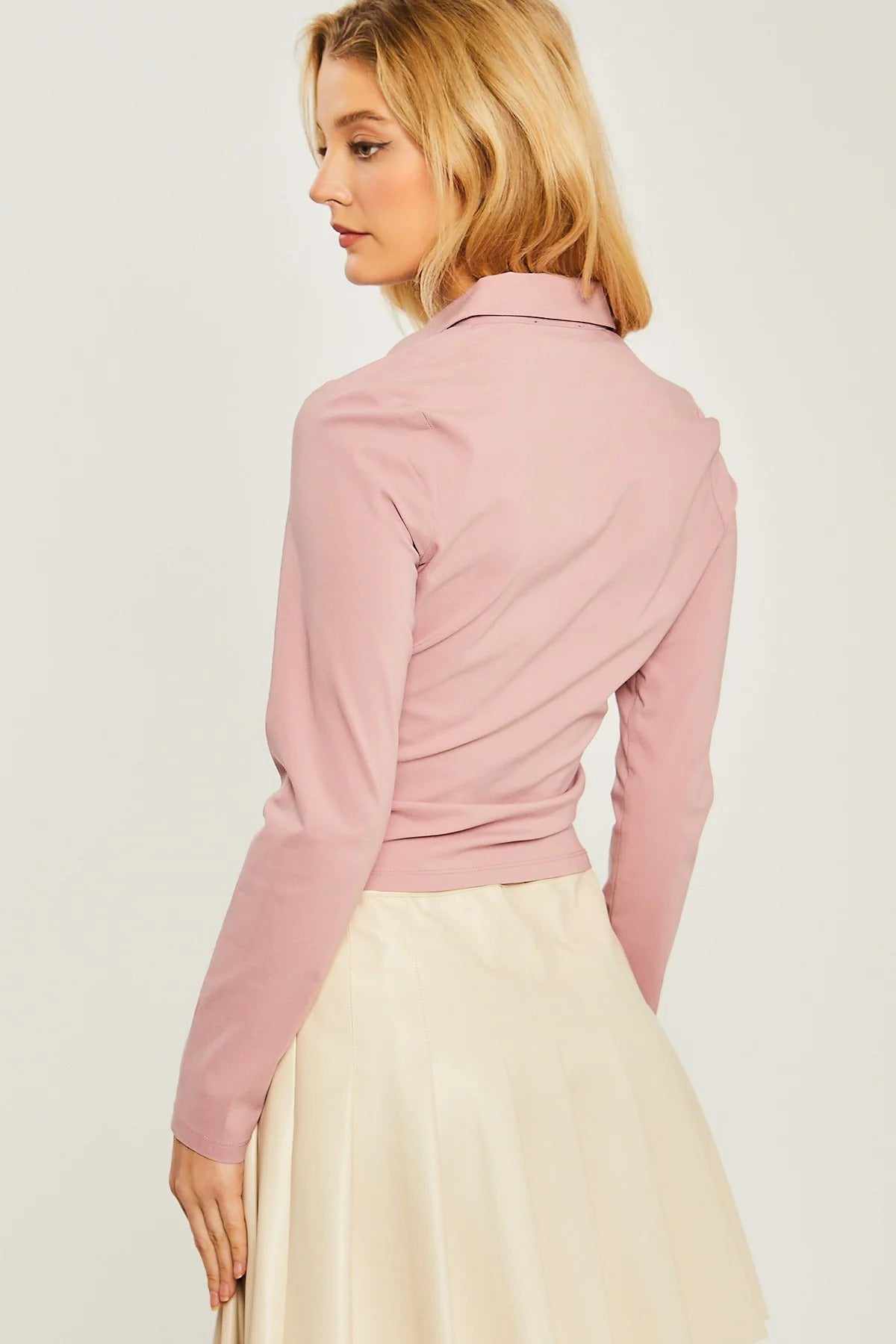 Woman wearing mauve woven solid ruched front long sleeve top, paired with a cream skirt, shown from the back.