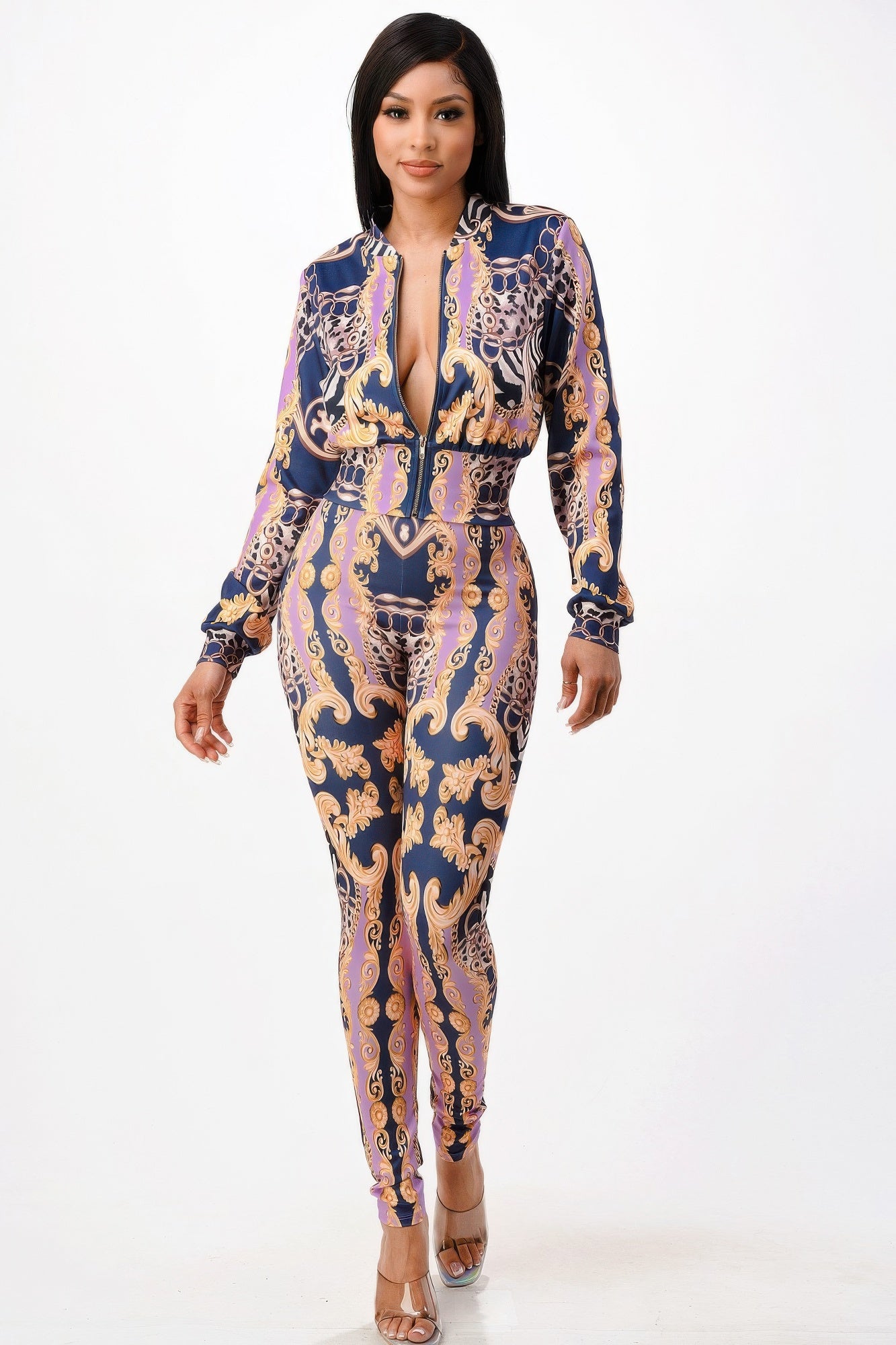 Woman in form-fitting baroque print jumpsuit with deep V-neck, featuring navy blue base with gold, purple and chain patterns. She poses against...