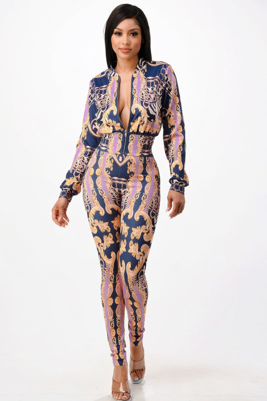 Woman in form-fitting baroque print jumpsuit with deep V-neck, featuring navy blue base with gold, purple and chain patterns. She poses against...